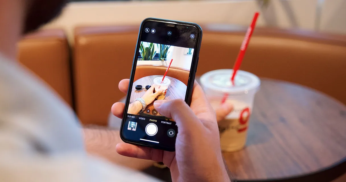 Pessoa fotografando um copo de bebida com o celular em uma cafeteria